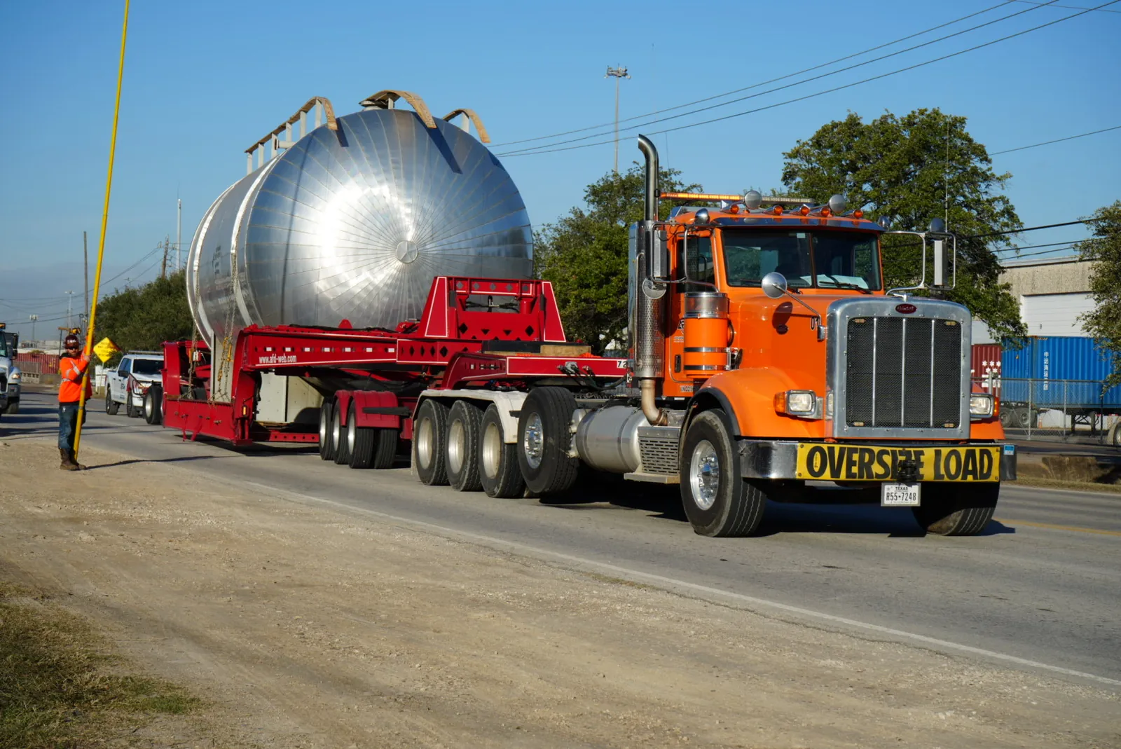Orange heavy-haul truck with an Oversize Load banner pulling a large silver tank on a multi-axle trailer