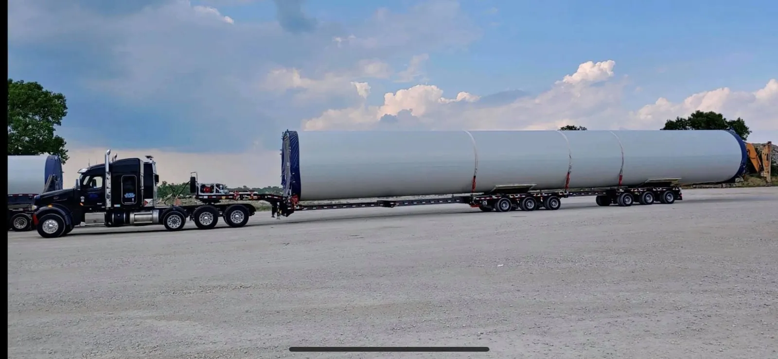 Truck hauling a long white cylindrical vessel on an extendable trailer