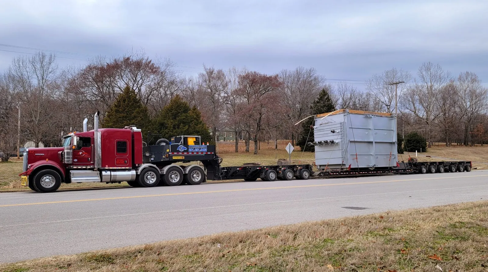 Red semi truck hauling large transformer on trailer