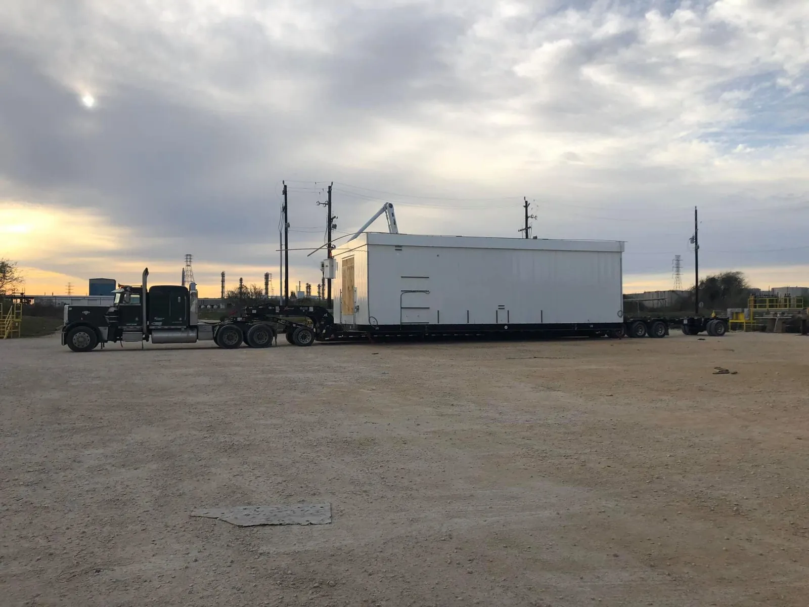 Semi truck with a white enclosed building module on a trailer at a yard