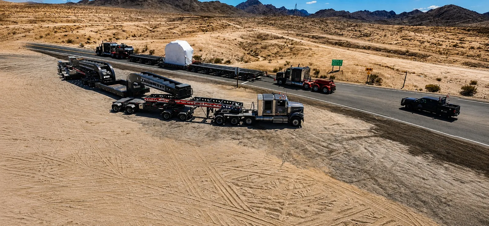 Drone view of a heavy haul convoy with a white wrapped load and an escort truck on a desert highway